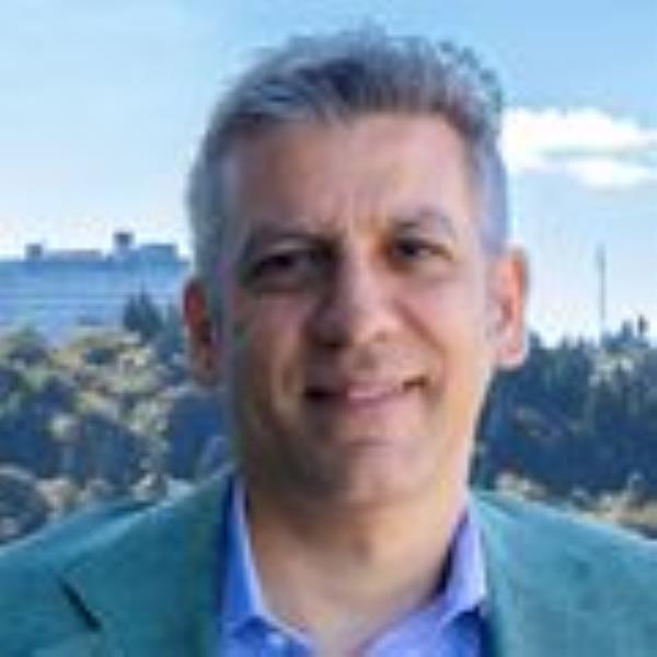 Steven Mansoor, M.D., Ph.D. stands atop the Center for Health and Healing building with the OHSU tram and Marquam hill viewable in the distance.